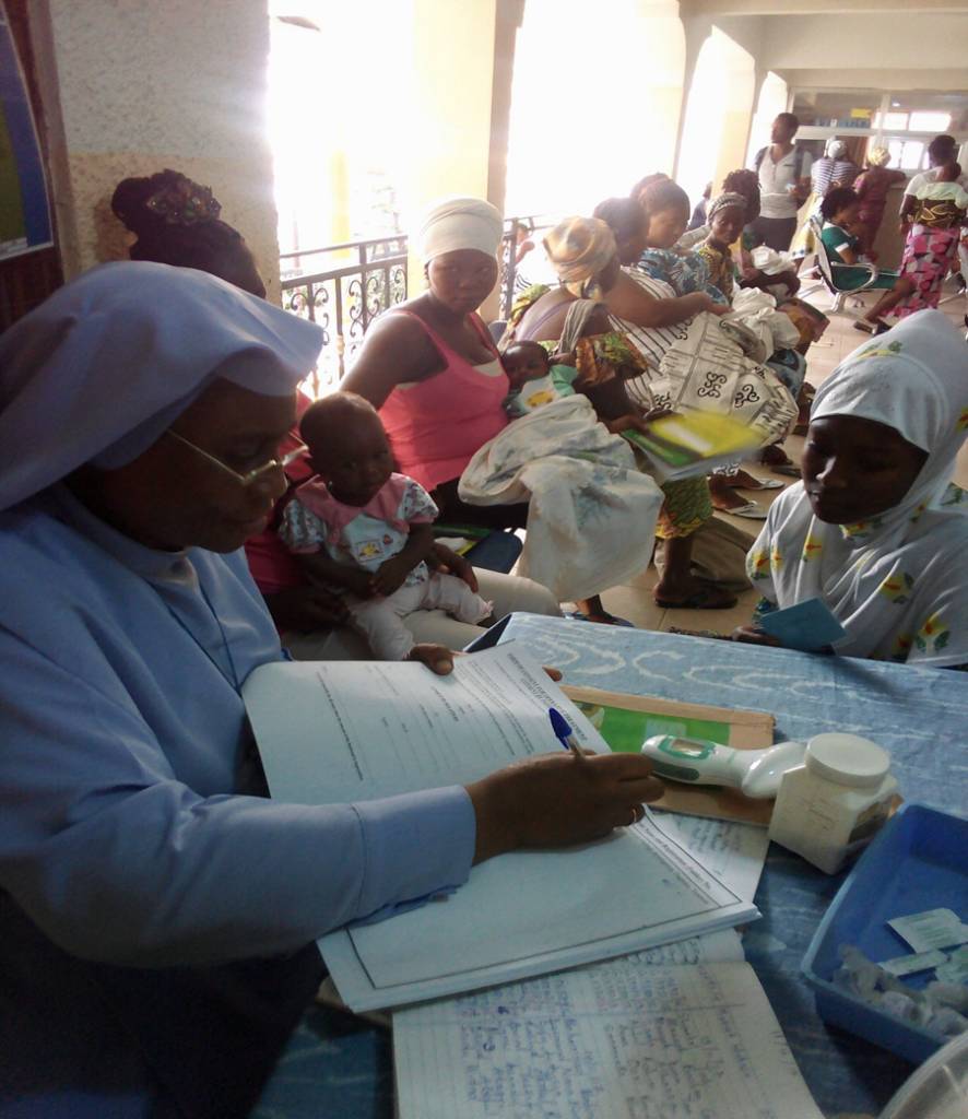 An IHM Sister keeping records at a clinic while mothers wait with their babies
